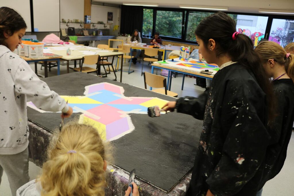 Schülerinnen malen gemeinsam an einem großen, bunten Kunstprojekt.
