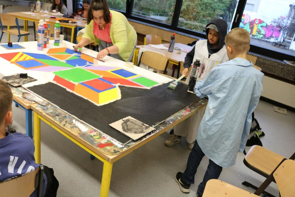 Schüler und Lehrer malen gemeinsam an einem Tisch mit bunten Farben.