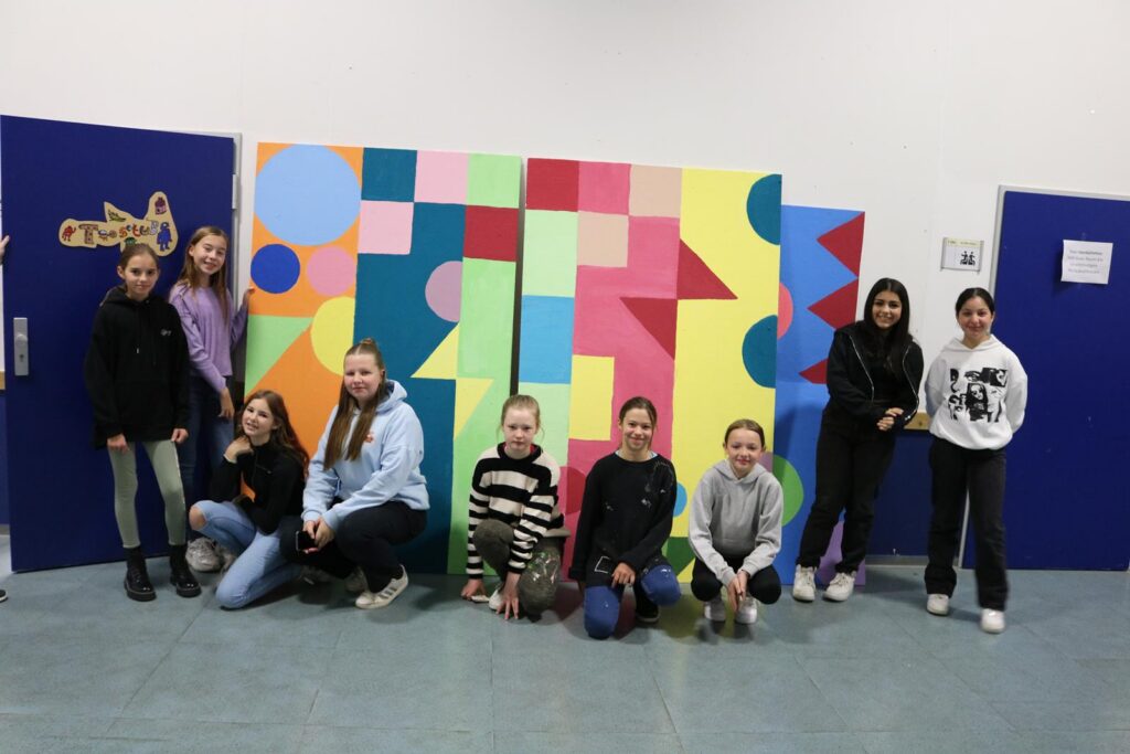 Gruppe von Schülerinnen vor bunt gestalteter Wand.