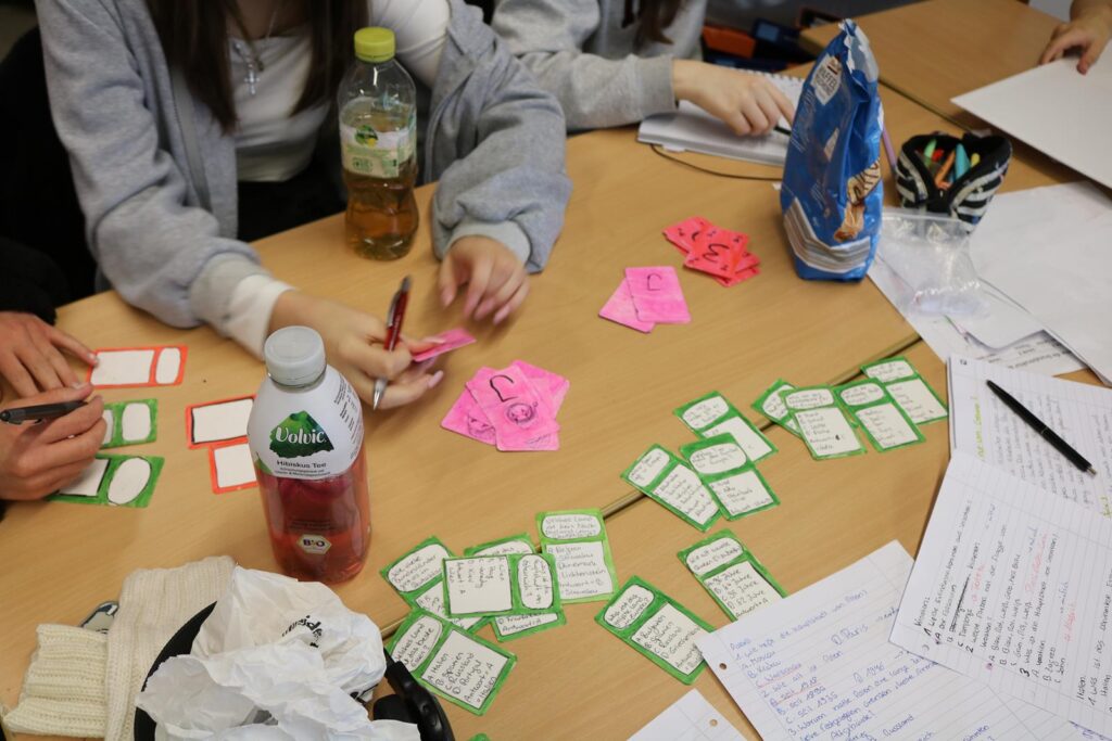 Schüler arbeiten an einem Tisch mit Karten, Getränken und Snacks.