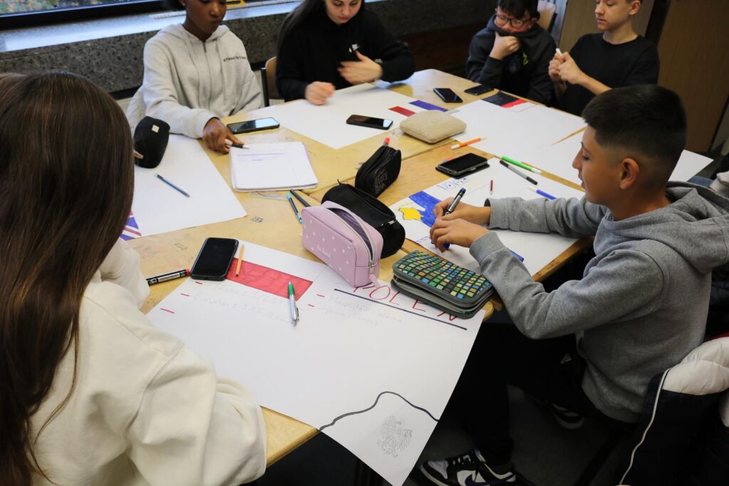Schüler arbeiten gemeinsam an einem Tisch mit Papier und Schreibutensilien.