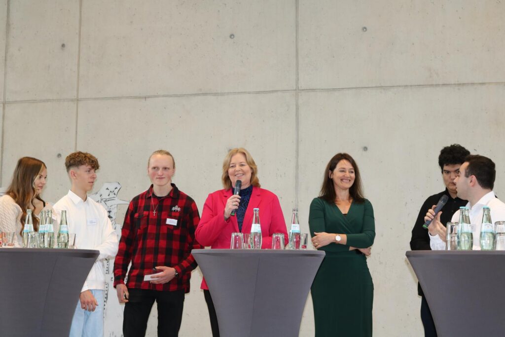 Gruppendiskussion mit mehreren Personen an einem Stehtisch in einem modernen Raum.