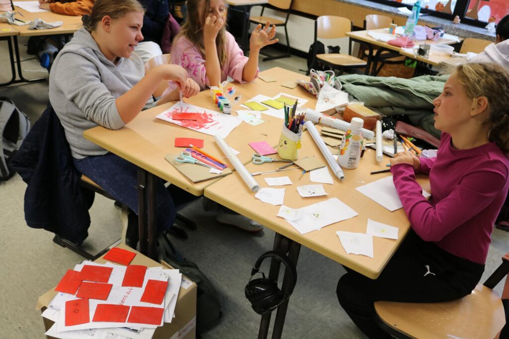 Vier Kinder arbeiten an einem Tisch mit Bastelmaterialien in einem Klassenraum.