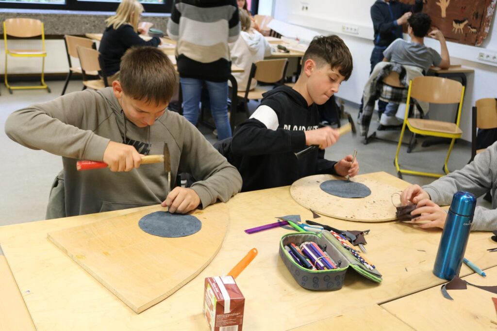 Zwei Schüler arbeiten an Holzprojekten in einem Werkraum.