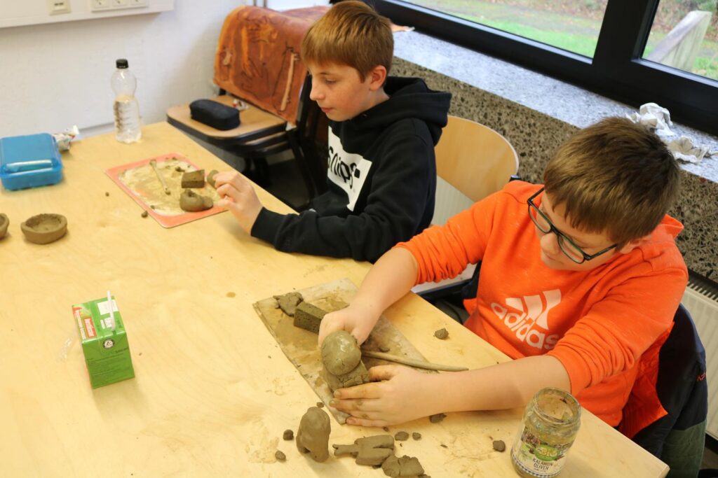 Zwei Schüler arbeiten an einem Bastelprojekt mit Ton in einem Klassenzimmer.