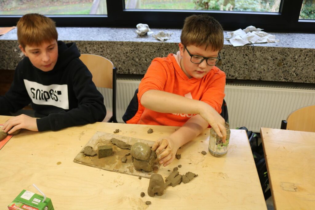 Zwei Schüler arbeiten kreativ mit Ton an einem Tisch.