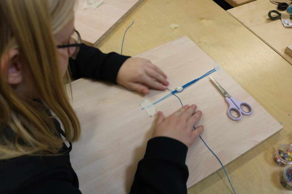 Schülerin arbeitet an einem Holzprojekt mit Schnur und Schere.