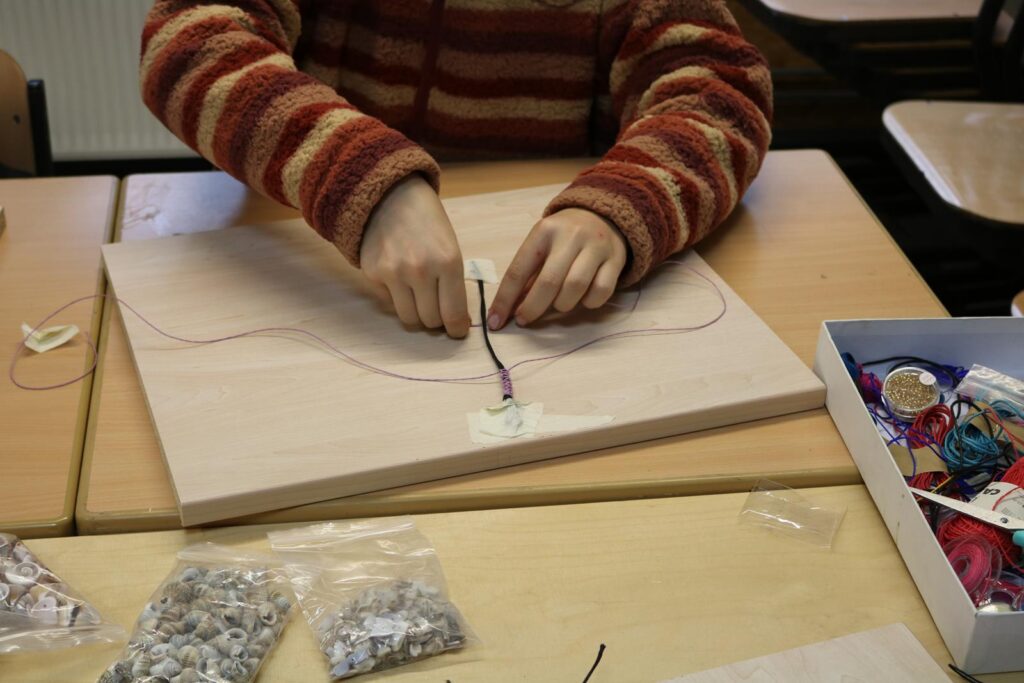 Ein Schüler bastelt mit Fäden und Materialien auf einem Tisch.