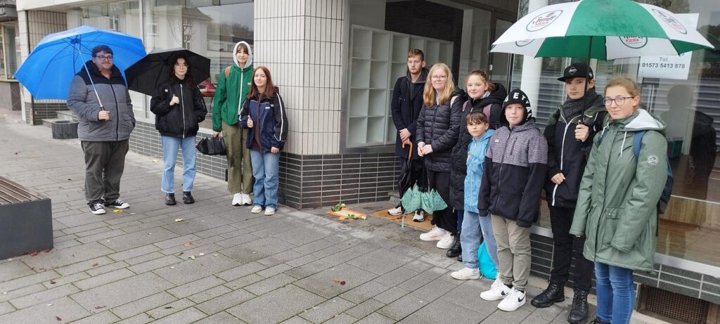 Gruppe von Personen mit Regenschirmen steht an einer Stadtstraße.