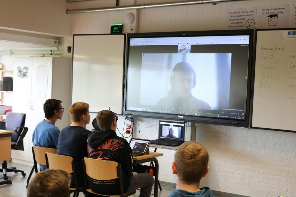 Schüler sitzen vor einem Bildschirm mit Videokonferenz.