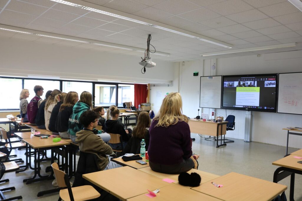 Schülerinnen und Schüler im Klassenraum schauen auf einen Bildschirm.