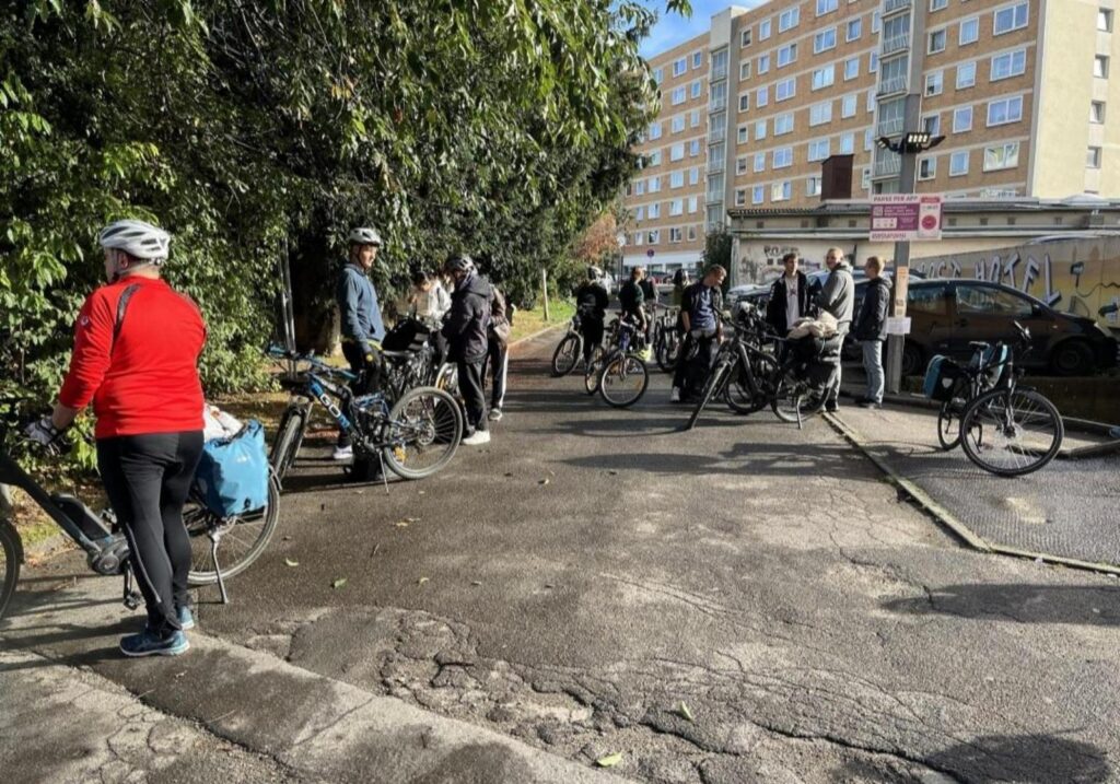 Eine Gruppe von Radfahrern hält an einer Straße, umgeben von Bäumen und Gebäuden.