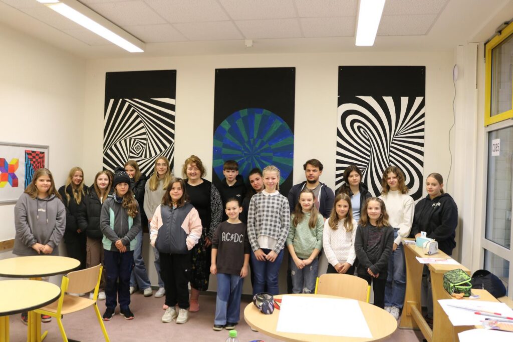 Gruppe von Schülerinnen und Schülern in einem Klassenraum mit dekorativen Wandbildern.