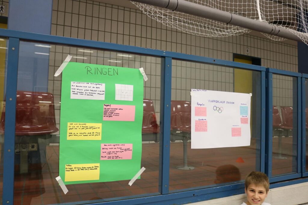 Plakate an einer Wand in der Turnhalle, ein Junge sitzt darunter.