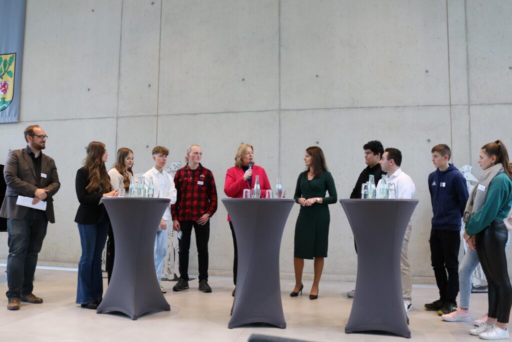 Gruppe von Personen steht an Stehtischen in einem Raum mit grauen Wänden.