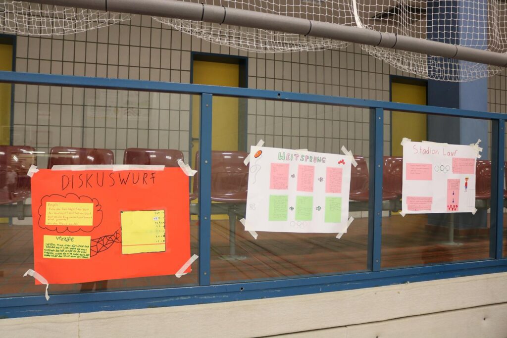 Bunte Plakate an einem Geländer in einer Sporthalle.