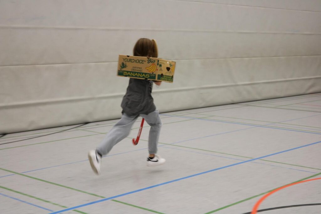 Ein Kind läuft mit einem Holzschild in der Sporthalle.