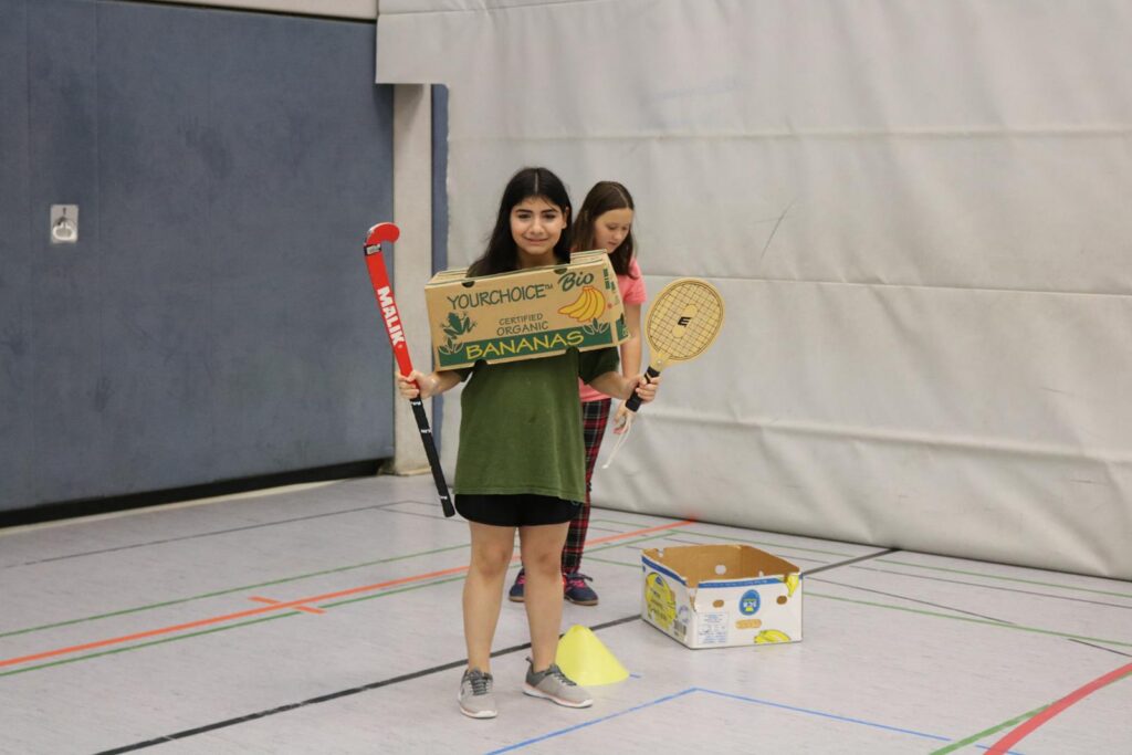 Mädchen in Turnhalle mit einem Schild und Sportgeräten.