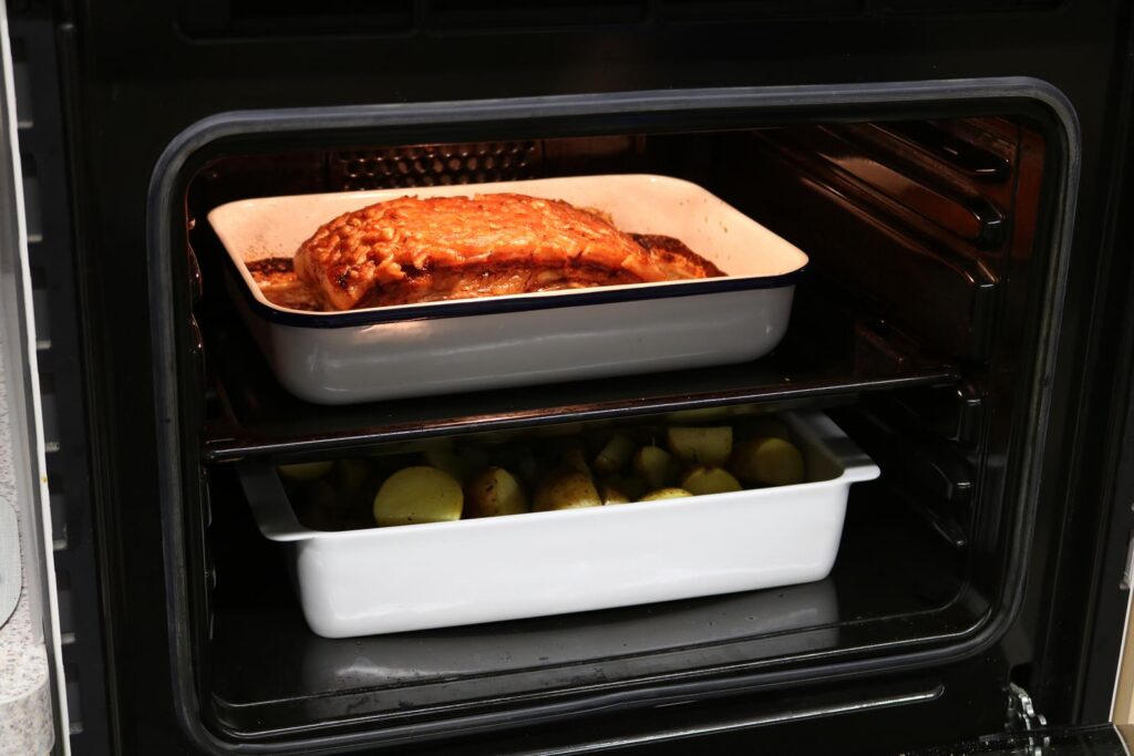 Fleischgericht und Gemüse in zwei Auflaufformen im Backofen.