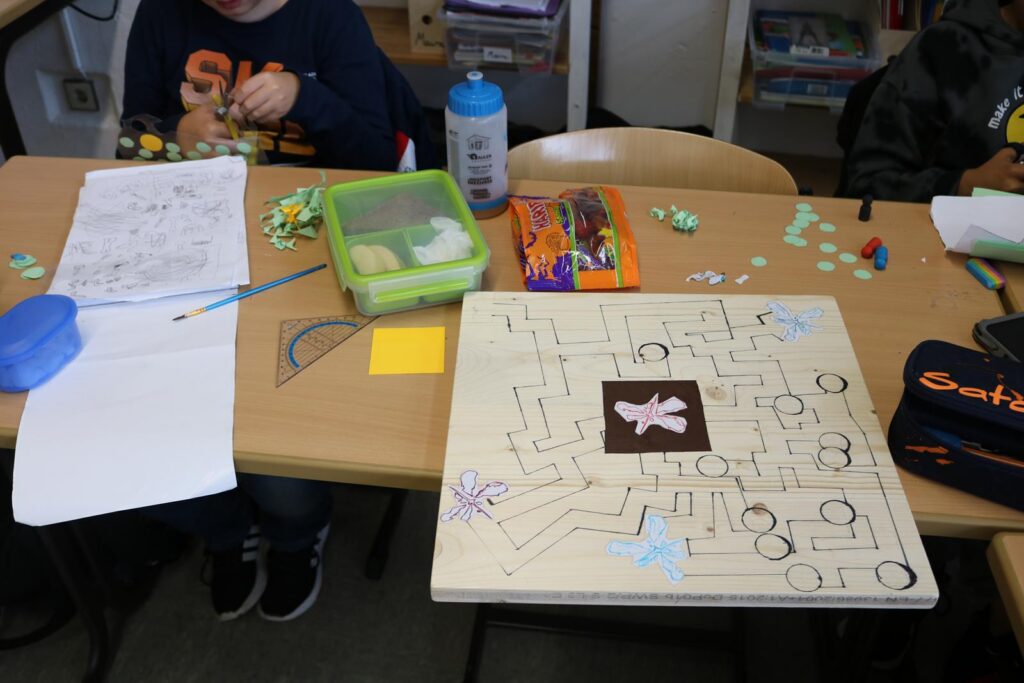 Schreibtisch mit Bastelmaterialien und einem Spielbrett aus Holz.