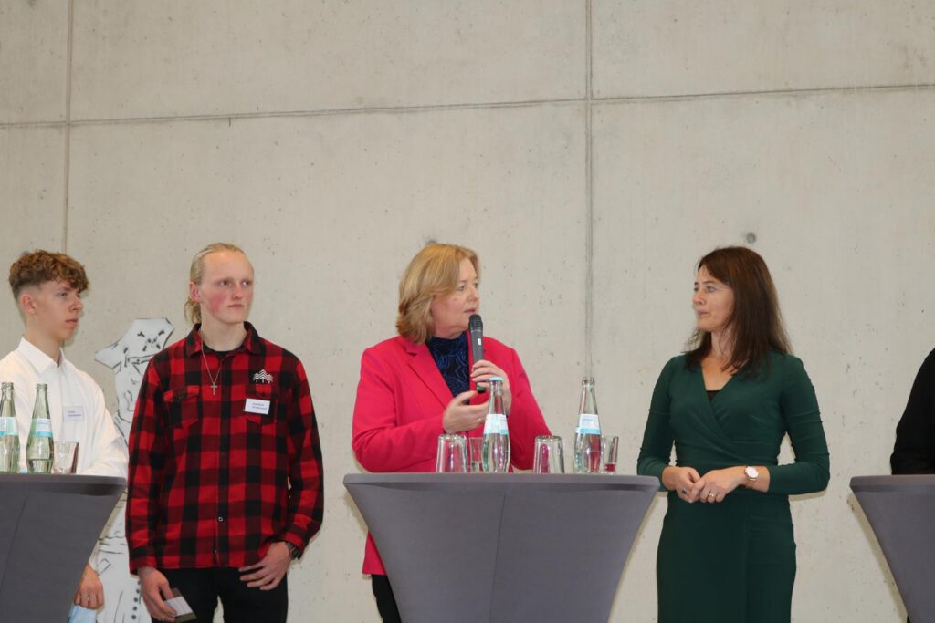 Vier Personen stehen an Stehtischen und unterhalten sich.