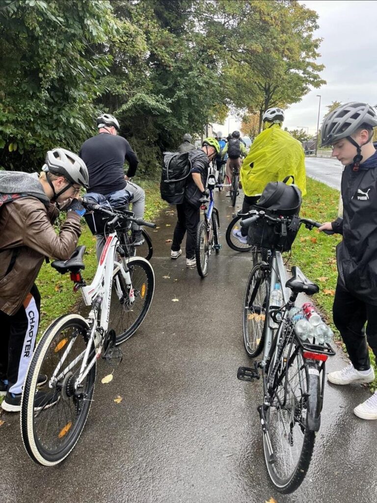 Gruppe von Radfahrern hält an einem Radweg, einige prüfen ihre Fahrräder.