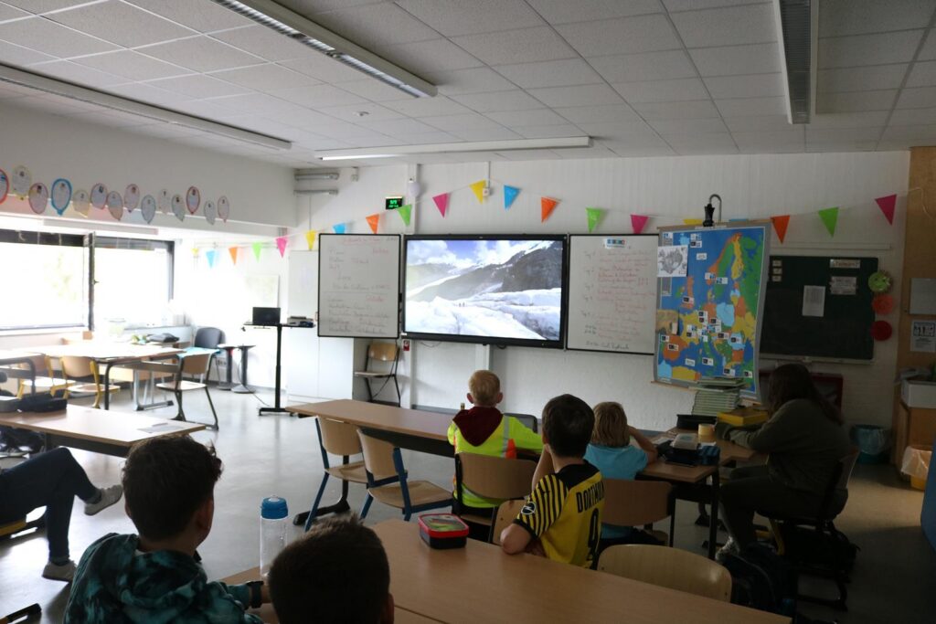 Schüler sitzen im Klassenraum und schauen auf einen Bildschirm mit einer Präsentation.