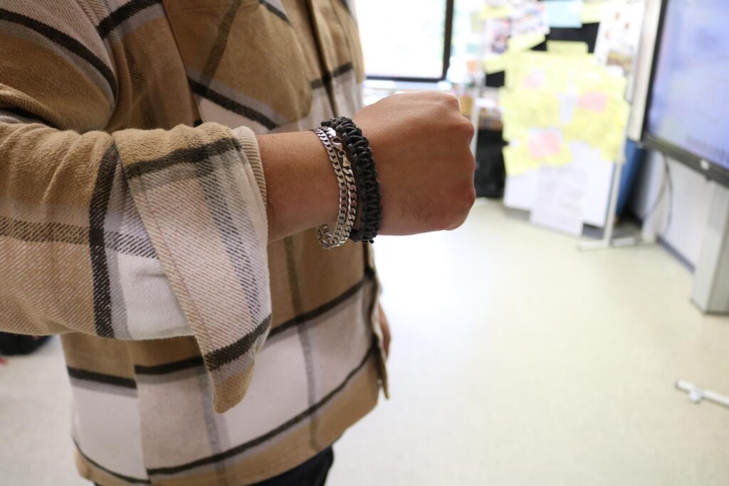 Ein Arm mit mehreren Armbändern auf einem Hintergrund aus Büromaterialien.