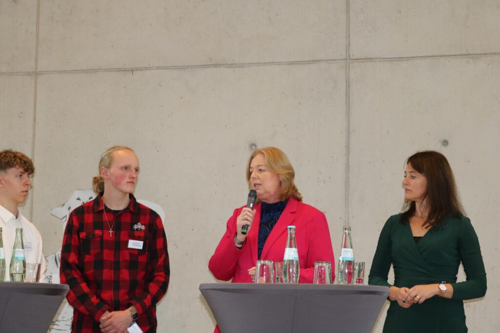 Drei Personen stehen an einem Stehtisch und sprechen miteinander.