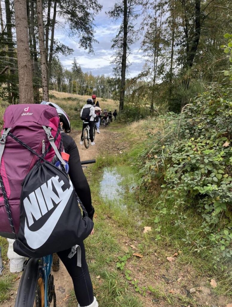 Gruppe von Radfahrern auf einem schmalen Waldweg mit Pflanzen und einem Pfütze.