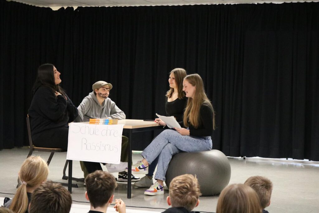 Schüler führen ein Theaterstück auf einer Bühne vor Publikum auf.