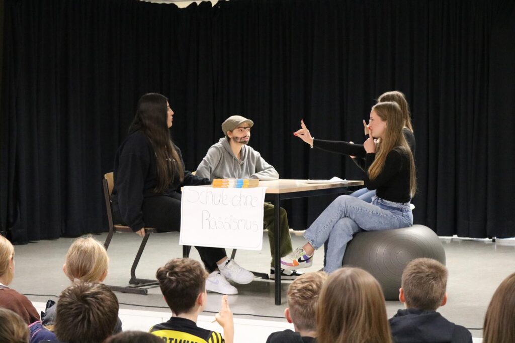 Eine Schülergruppe führt eine Diskussion auf einer Bühne vor Publikum.