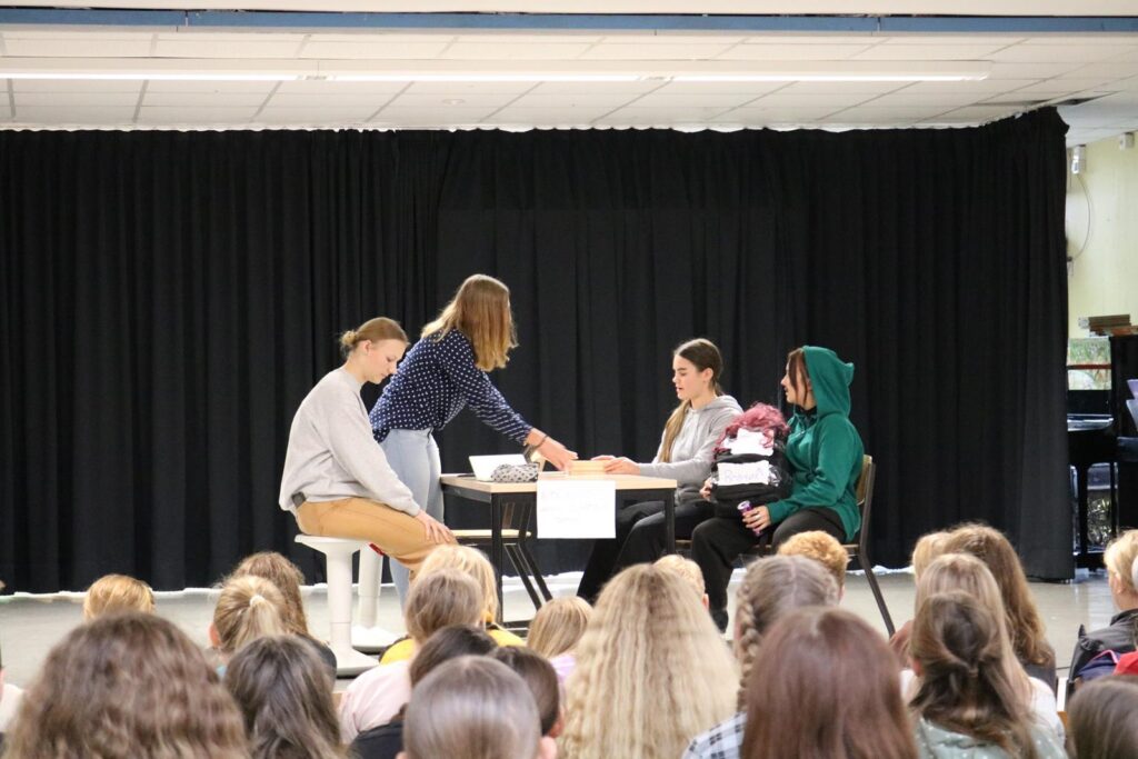 Schüler führen eine Schauspielaufführung auf einer Bühne vor Publikum auf.