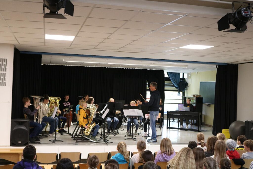 Schülerorchester spielt auf der Bühne vor Publikum in einem Musikraum.