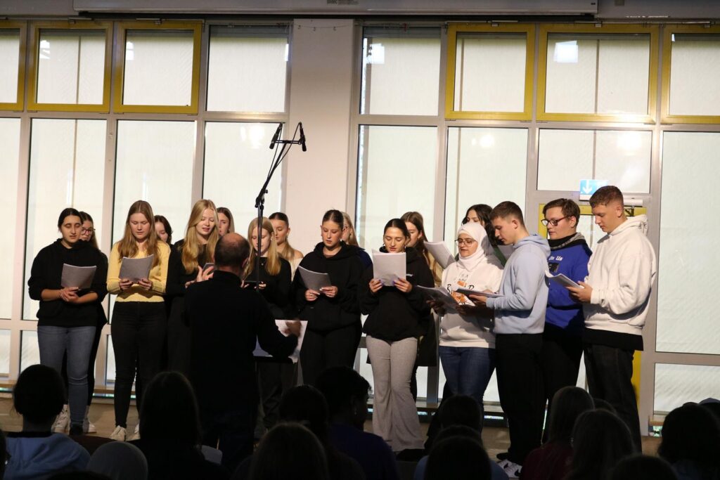 Schülerinnen und Schüler singen in einem Chor vor Publikum.