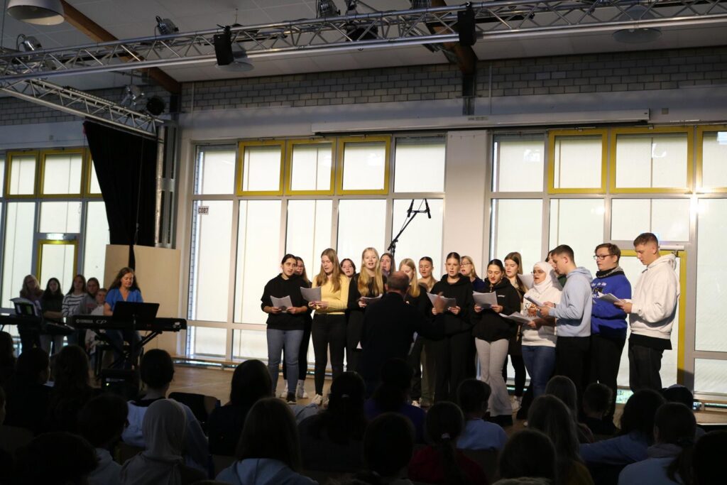 Schülerchor steht auf der Bühne und singt vor Publikum.