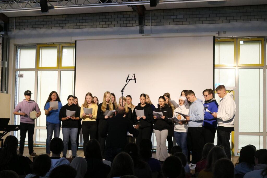 Schülerinnen und Schüler stehen auf der Bühne und singen vor Publikum.