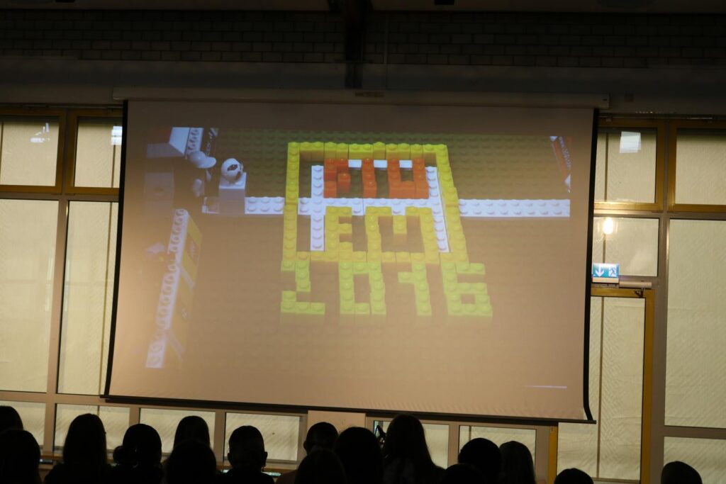 Eine Projektion mit bunten LEGO-Steinen und der Aufschrift "AM 2016". Zuschauer im Hintergrund.