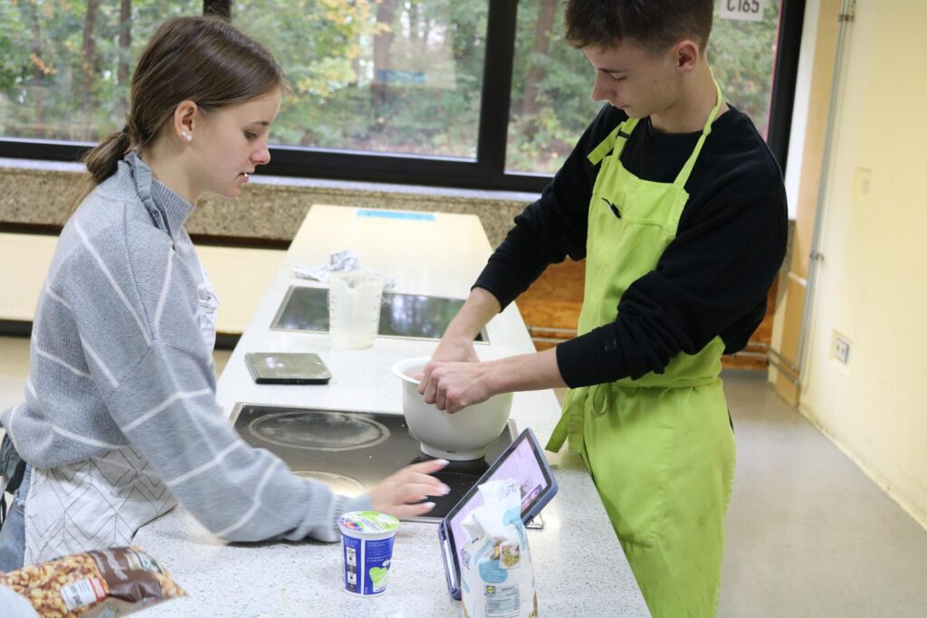 Zwei Schüler bereiten in einer Küche gemeinsam eine Mahlzeit vor.
