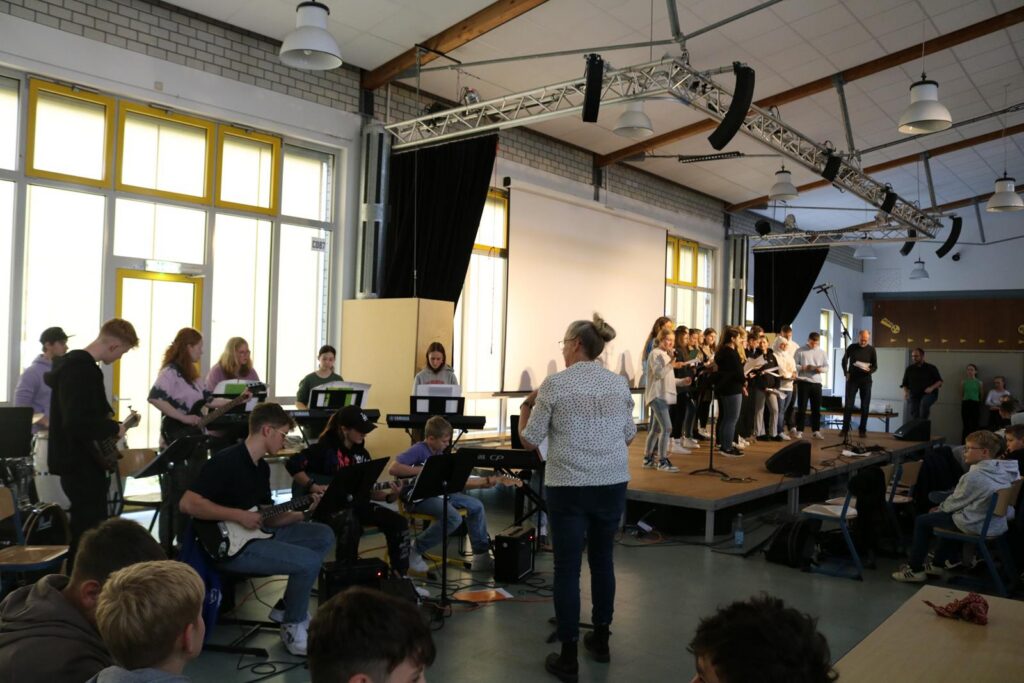 Schülerinnen und Schüler stehen auf einer Bühne, während eine Band spielt.