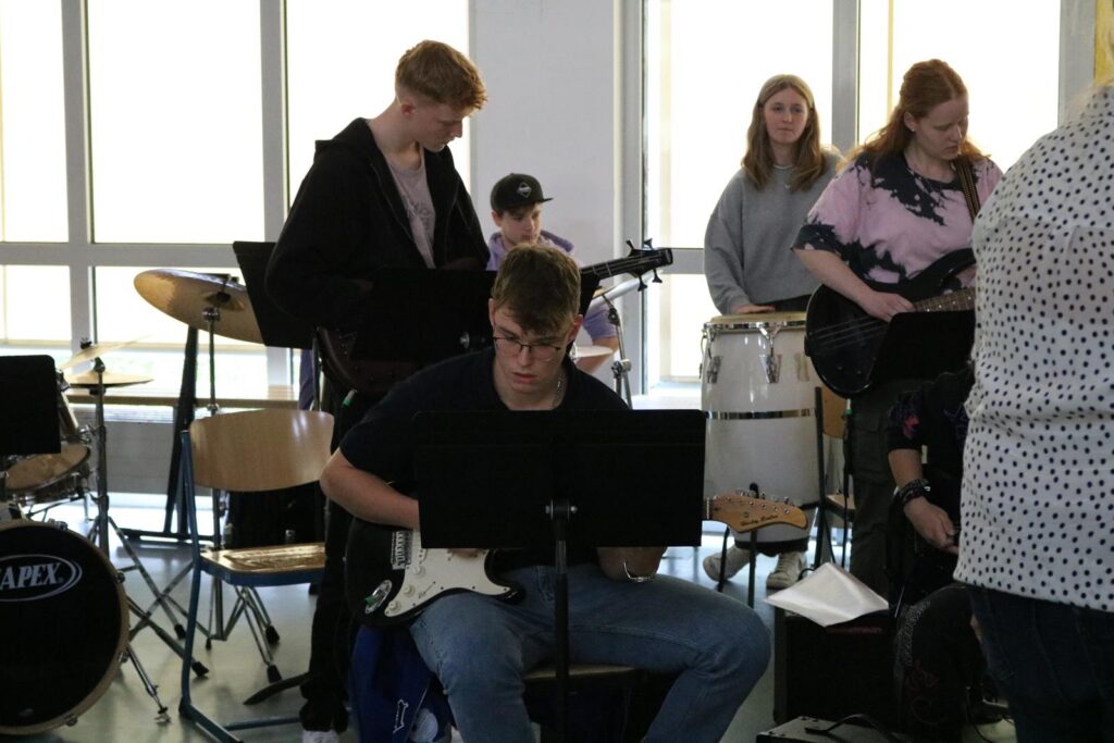 Schüler spielen in einer Band mit Instrumenten und Notenständern.