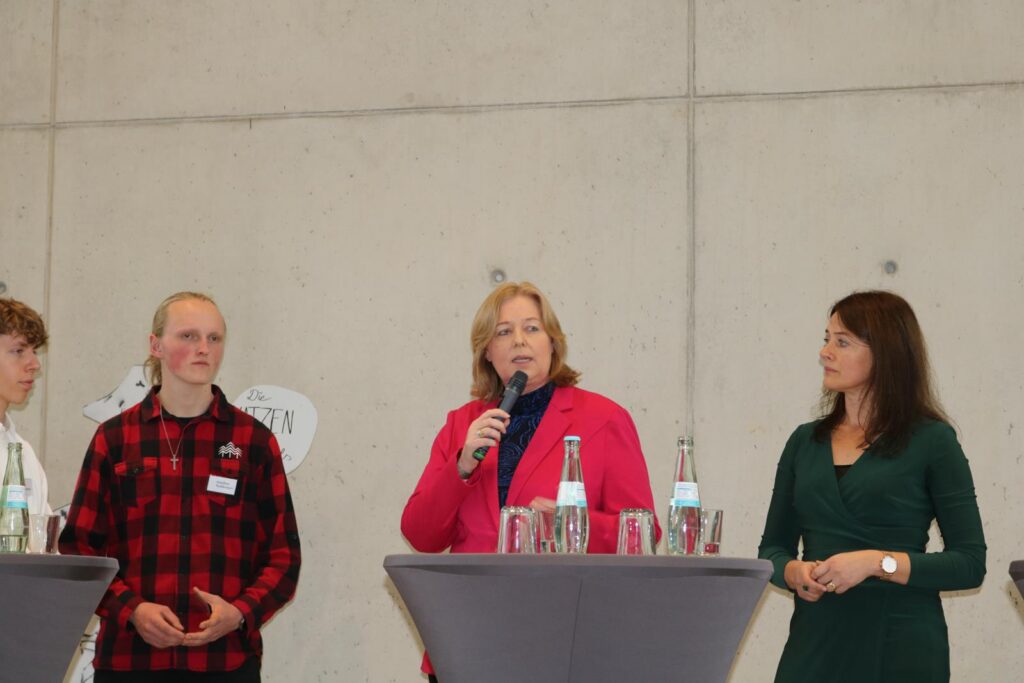 Drei Personen bei einer Diskussionsrunde stehen an Stehtischen.