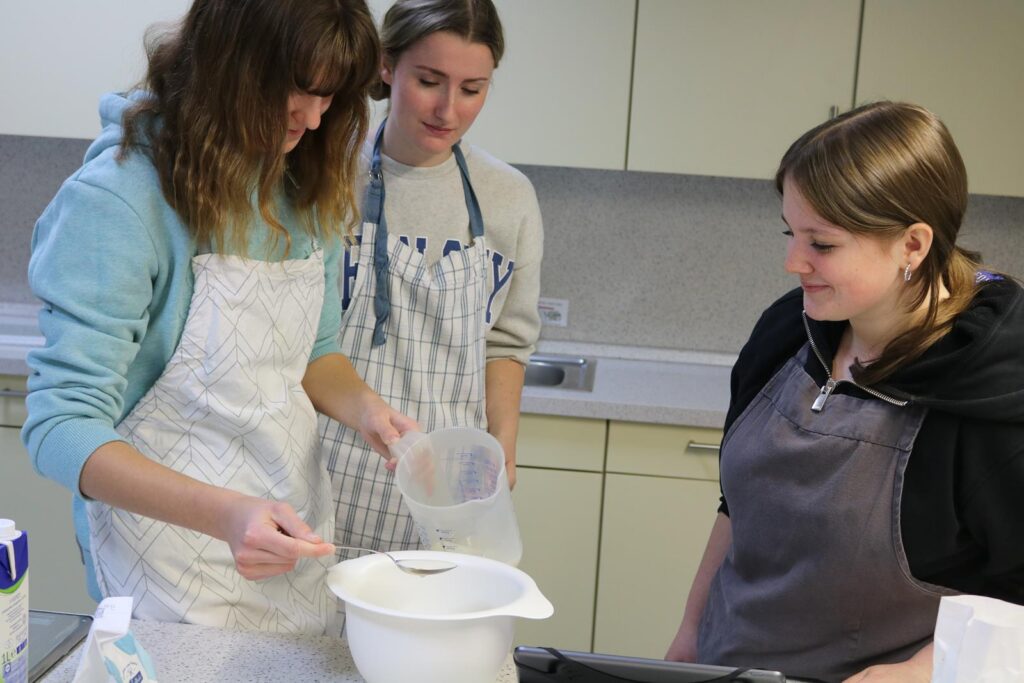 Drei Schülerinnen backen zusammen in einer Schulküche.