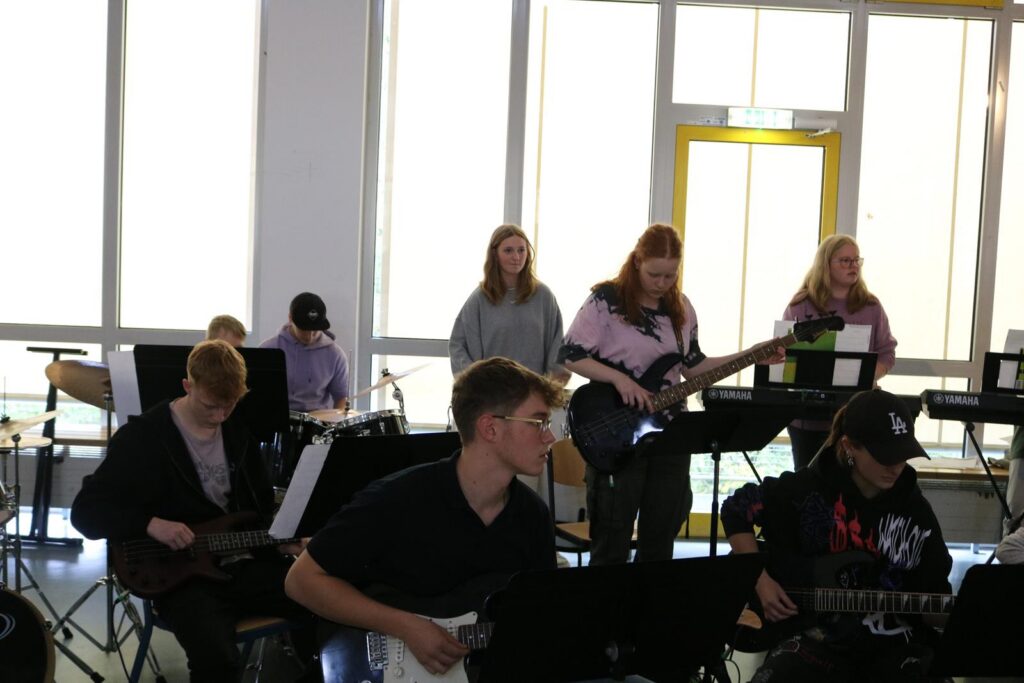 Schülerinnen und Schüler spielen in einer Band mit Gitarren und Schlagzeug.