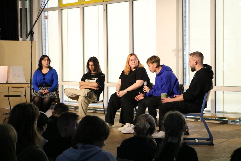 Podiumsdiskussion mit fünf Personen auf einer Bühne vor Publikum.