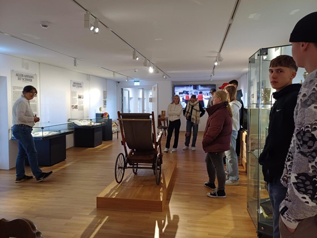 Besucher im Museum stehen vor einer historischen Kutsche in einem Ausstellungsraum.