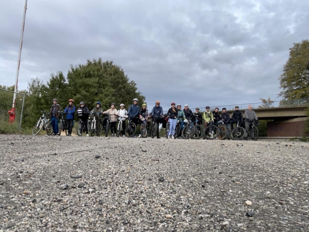 Gruppe von Radfahrern steht auf einem Schotterweg unter bewölktem Himmel.