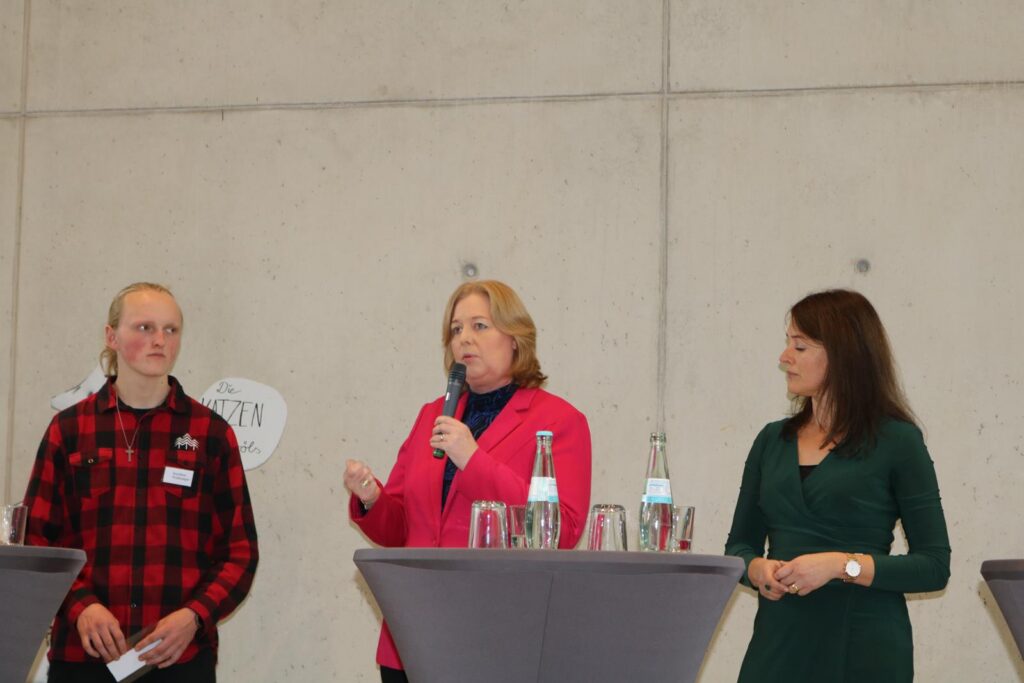 Drei Personen stehen an Stehtischen und diskutieren.