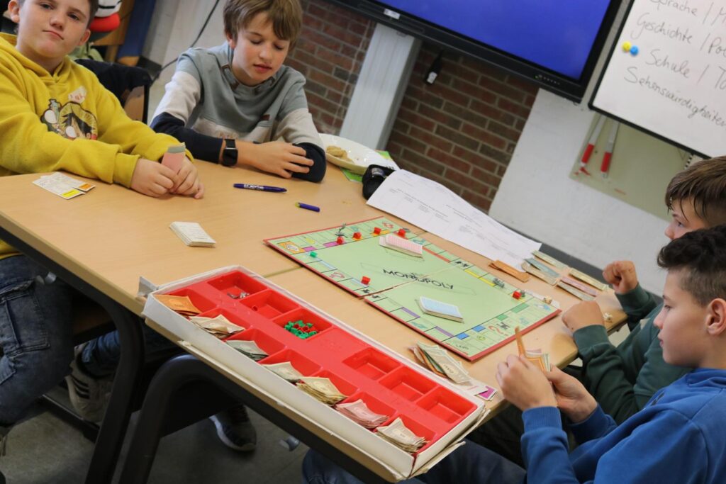 Vier Kinder sitzen an einem Tisch und spielen Monopoly.
