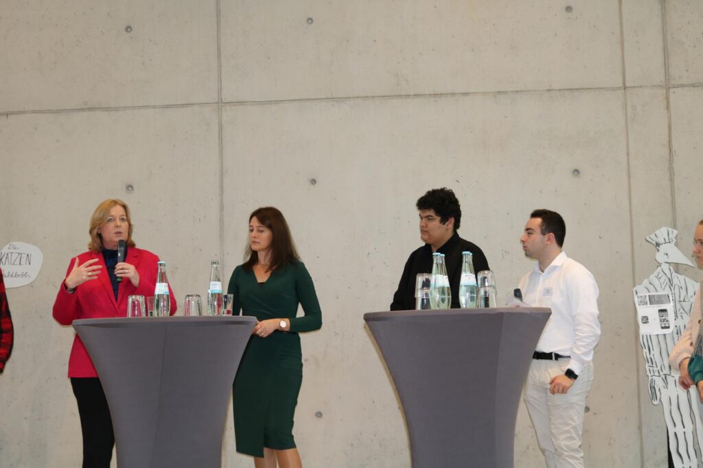 Vier Personen stehen an Stehtischen und sprechen miteinander in einer modernen Umgebung.